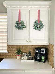 two wreaths are hanging on the cabinets above a coffee maker