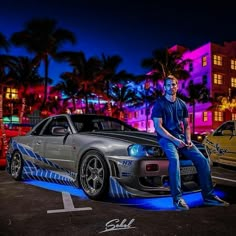 a man sitting on the hood of a car in a parking lot with other cars