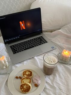 an open laptop computer sitting on top of a bed next to two cups of coffee