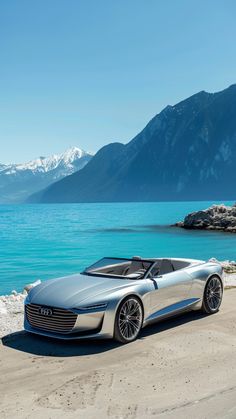 a silver car parked on the side of a road next to water with mountains in the background