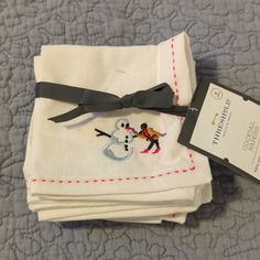 four white napkins with embroidered snowmen on them and a black ribbon tied around the edges