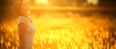 a woman standing in a field with her eyes closed and the sun shining behind her