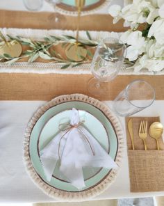 a place setting with napkins, silverware and white flowers on the table cloth