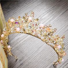 a gold tiara with pink flowers and pearls on the headpiece is sitting on a wooden table