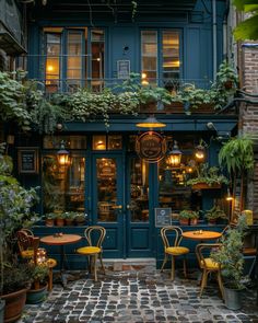 an outdoor patio with tables and chairs in front of a blue building filled with potted plants