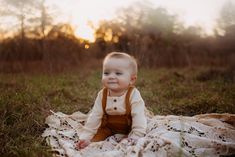 a baby is sitting on a blanket in the grass and smiling at the camera,