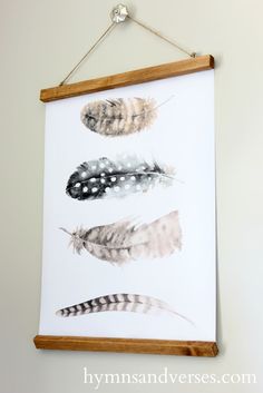 three feathers are hanging on the wall in front of a white background with a wooden frame