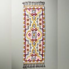 the wall hanging is decorated with multicolored designs and tasselled fringes