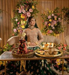 a woman sitting in front of a table with food on it and flowers behind her