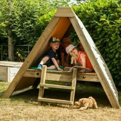 two children sitting in a wooden play structure with their dog laying on the ground next to them