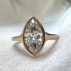 a ring with a pear shaped diamond in it on a white cloth covered tablecloth