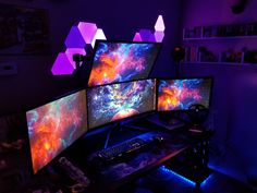 three computer monitors sitting on top of a desk in front of a purple wall with lights