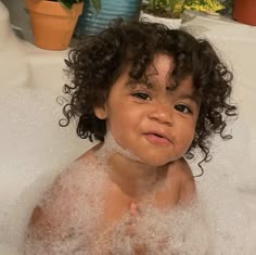 a young child sitting in a bathtub with bubbles on his face and chest, smiling at the camera