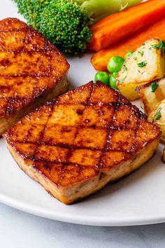 some meat and vegetables on a plate with broccoli, carrots and peas