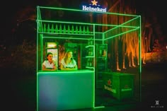 a lit up kiosk sitting on the side of a road at night with people in it