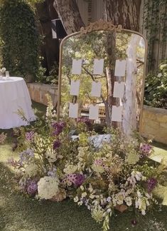 a mirror sitting on top of a lush green field next to a table covered in flowers