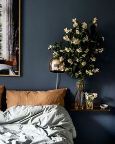 a bedroom with blue walls and white flowers in a vase on the nightstand next to the bed