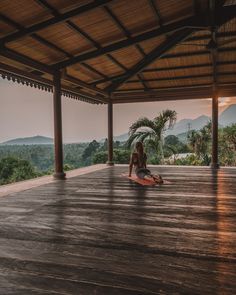 a woman sitting on top of a wooden floor next to a lush green forest covered hillside