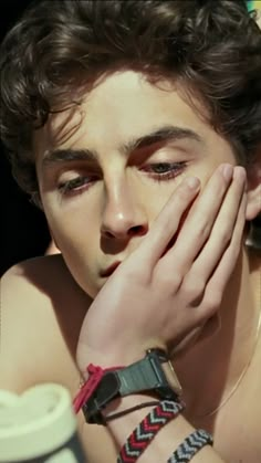 a shirtless man holding his hands to his face and looking at the camera while wearing bracelets