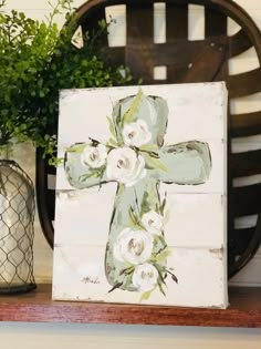 a wooden cross with white flowers painted on it sitting next to a potted plant