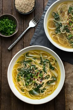 two bowls of soup with noodles, spinach and other ingredients on a wooden table