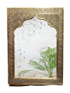 an ornate gold framed mirror with a palm tree in the middle and a white brick wall behind it