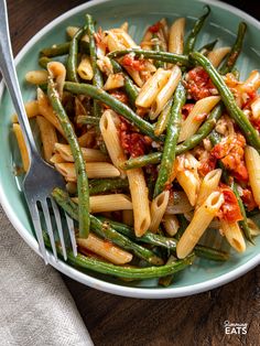 pasta with green beans and tomato sauce in a blue bowl on a wooden table next to a fork