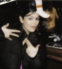 a woman wearing a white hat and black jacket posing for a photo with her hands in the air