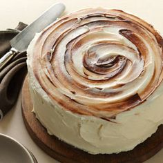 a close up of a cake with icing on a wooden platter next to utensils