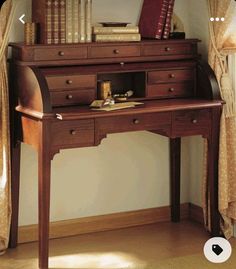 a wooden desk with books on top of it in front of a curtained window