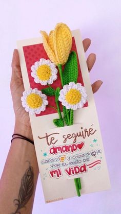 a person holding up a card with crocheted flowers on it and writing in spanish