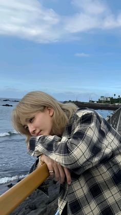 a woman leaning on a railing by the ocean with her hair in a bun and wearing a plaid shirt