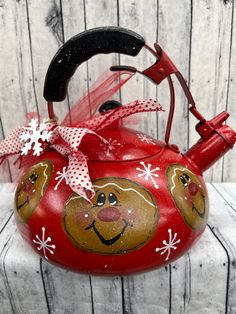 a red tea kettle with a face painted on it and a bow around the handle