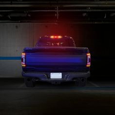 the back end of a blue pickup truck with its lights on in a parking garage