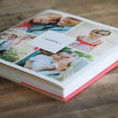 an open book with photos on it sitting on a wooden table next to a pen