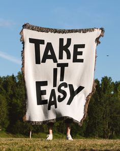 a person holding up a sign that says take it easy in front of some trees