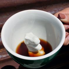 a person holding a cup filled with liquid and marshmallows on top of it