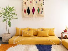 a bed with yellow pillows and colorful rugs in a white room next to a potted plant