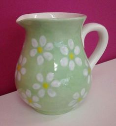 a green vase with white flowers painted on it