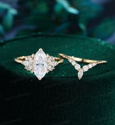 two gold rings with white diamonds on top of a green velvet hatbox, one is wearing