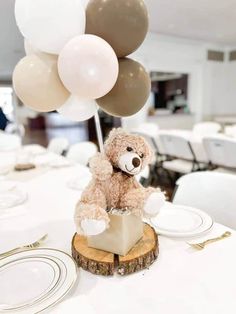 a brown teddy bear sitting on top of a wooden block with balloons in the background