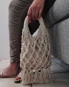 a woman is sitting on a couch holding a crocheted bag with tassels