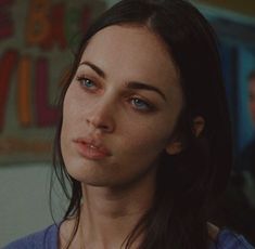 a woman with blue eyes and long black hair looks at the camera while standing in front of other people