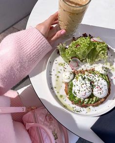 a person holding a drink over a white plate with food on it and a pink handbag