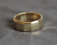 a close up of a gold wedding ring on a gray surface with the top half missing