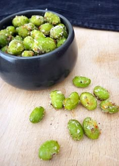 some green sprouts are in a black bowl on a table next to a wooden cutting board