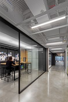 a woman sitting at a table in an office with lots of glass partitions on the walls