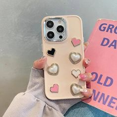 a person holding a phone case with hearts on it and an open book behind them