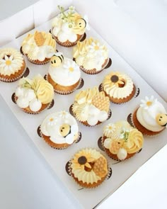 twelve cupcakes in a white box with yellow and brown frosting designs on them