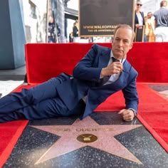 a man in a suit and tie laying on the hollywood walk of fame with his hand up to his face